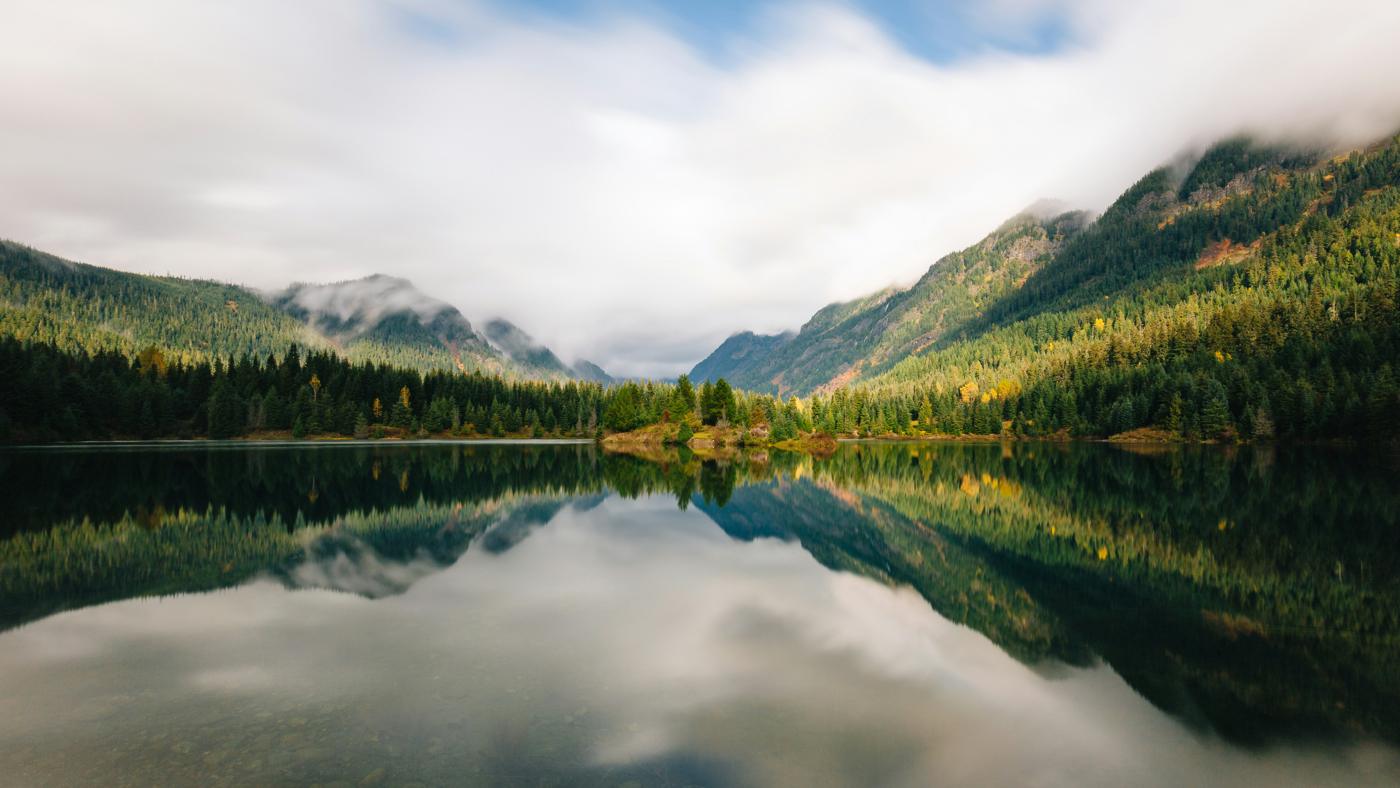 Still mountain lake reflecting clouds and forested hills