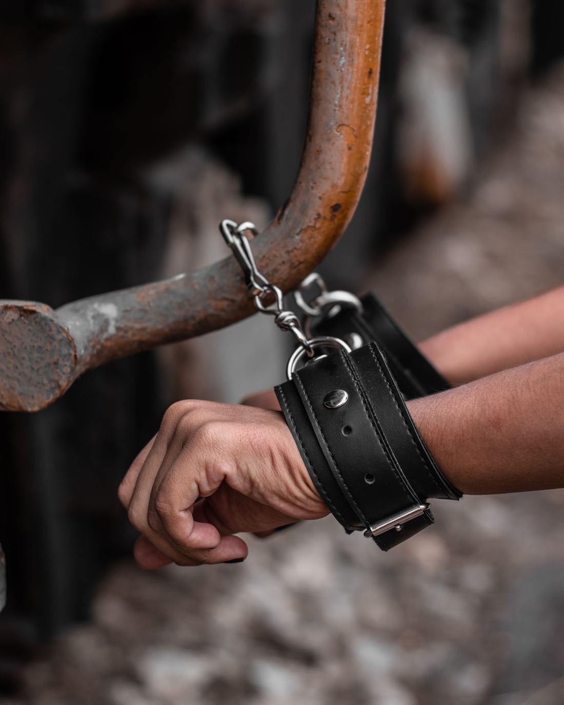 Two wrists in black leather cuffs clipped to a metal bar